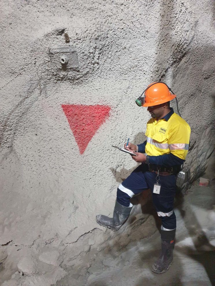 A PumpEng employee wearing a high-vis uniform and hard hat standing in an underground mine with a downwards red triangle painted on the wall for underground mine pump identification