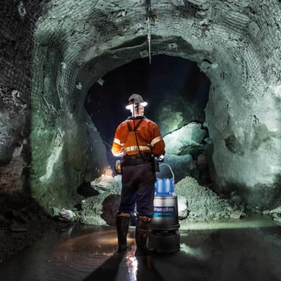 A man in high-vis uniform and helmet standing in an underground mine next to one of PumpEng's underground mine dewatering pumps, JetGuard