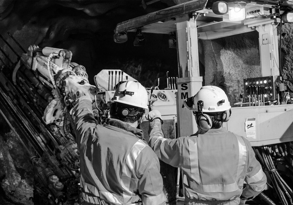Two underground mine workers standing next to mine machinery