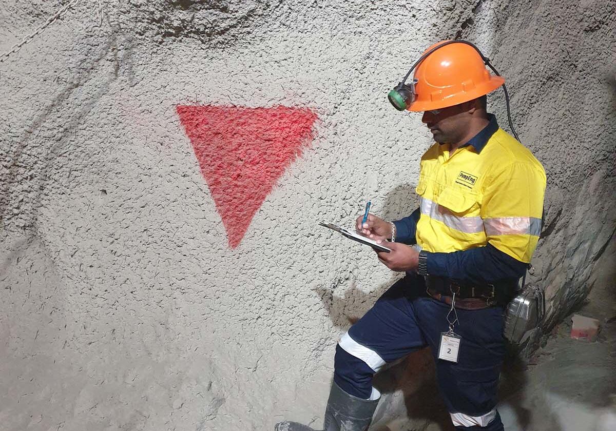 A PumpEng employee wearing a high-vis uniform and hard hat standing in an underground mine with a downwards red triangle painted on the wall for underground mine pump identification