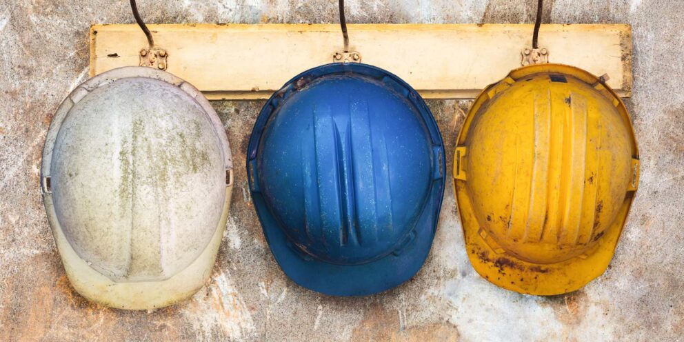 Three well-used mining helmets hanging on a rustic hook