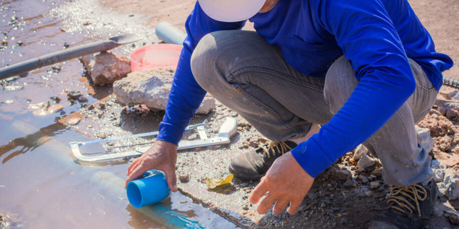 A person in a hardhat crouching near water.