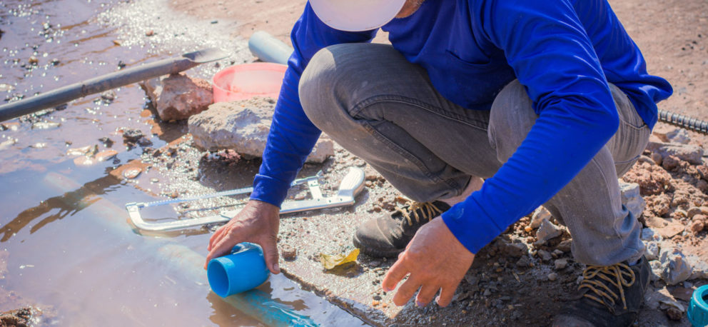 A person in a hardhat crouching near water.